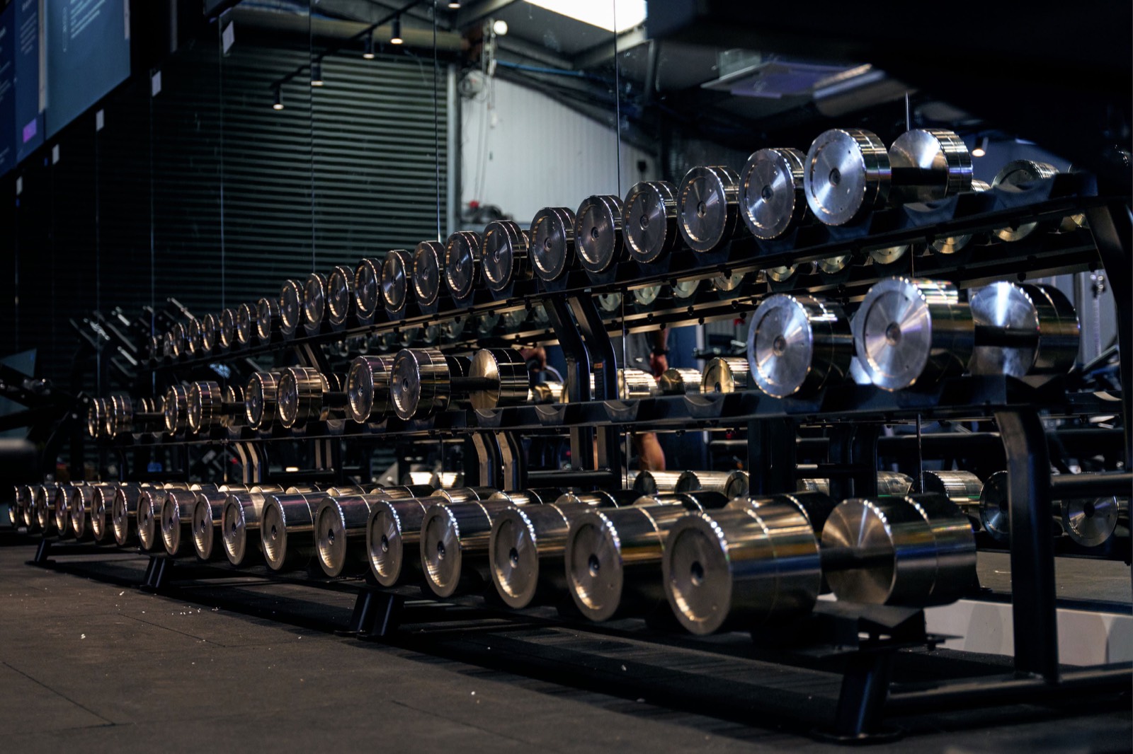 Rows of polished chrome dumbbells on black racks under low light at Swole Gym